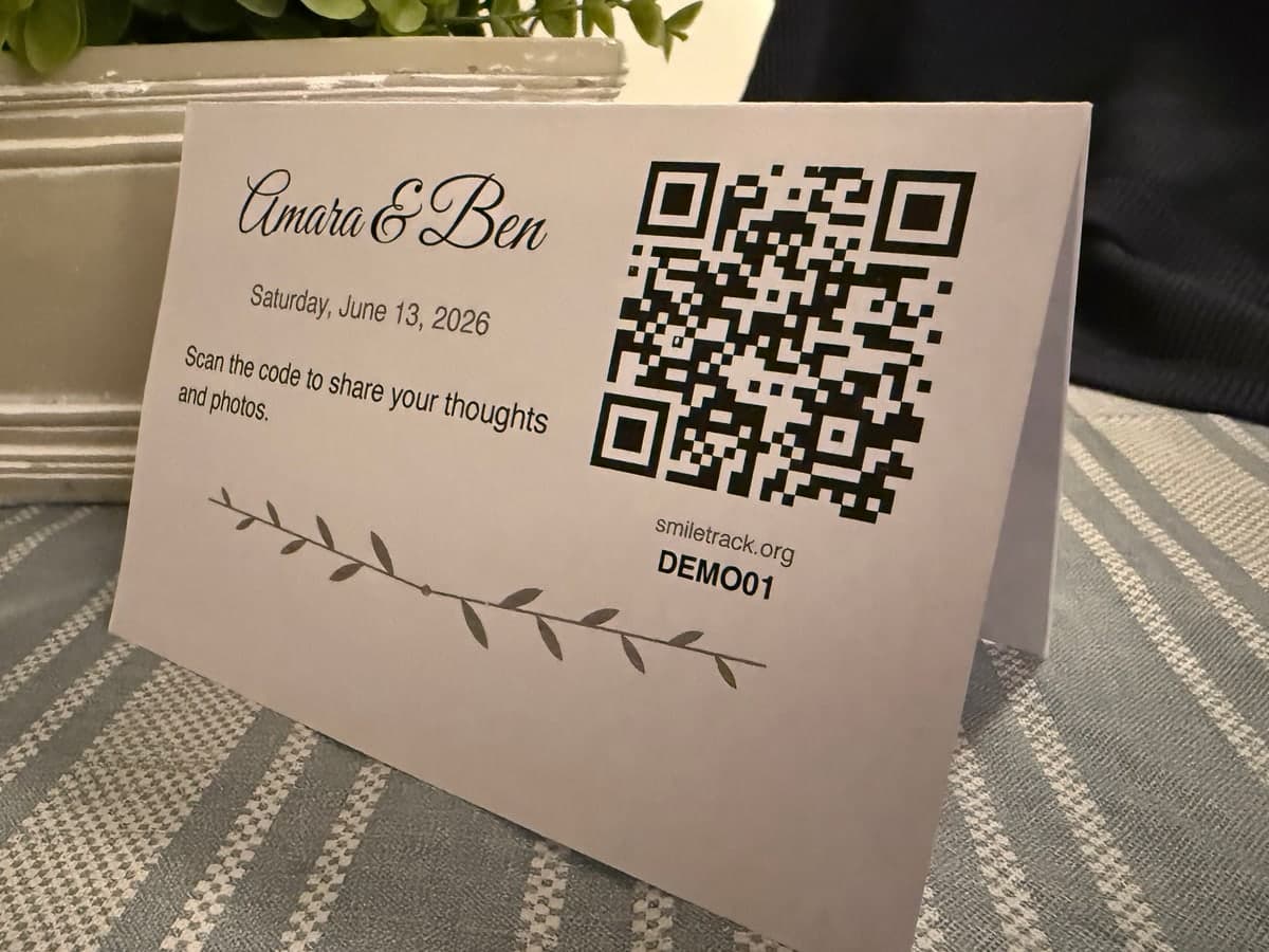A folded card standing on a table, reading 'Amara & Ben' with a QR code and an invitation to share photos